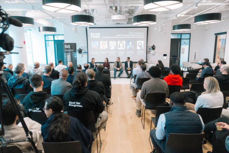 Panel discussion at the Bluefors Lab opening event in Chicago, with speakers seated on stage and an audience listening in a modern lab environment.