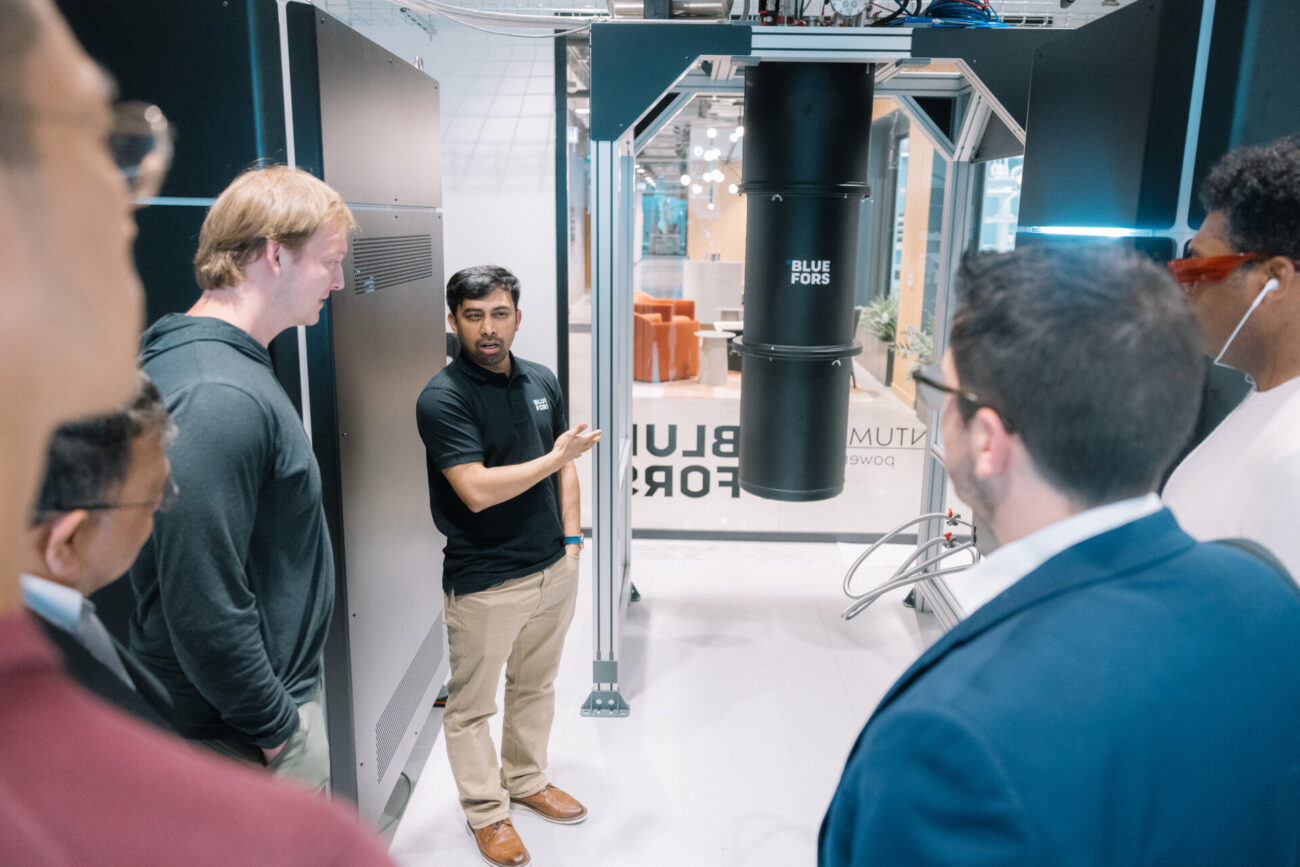 People discussing in a lab space at the Bluefors Lab opening event, with the cryogenic system in the background.