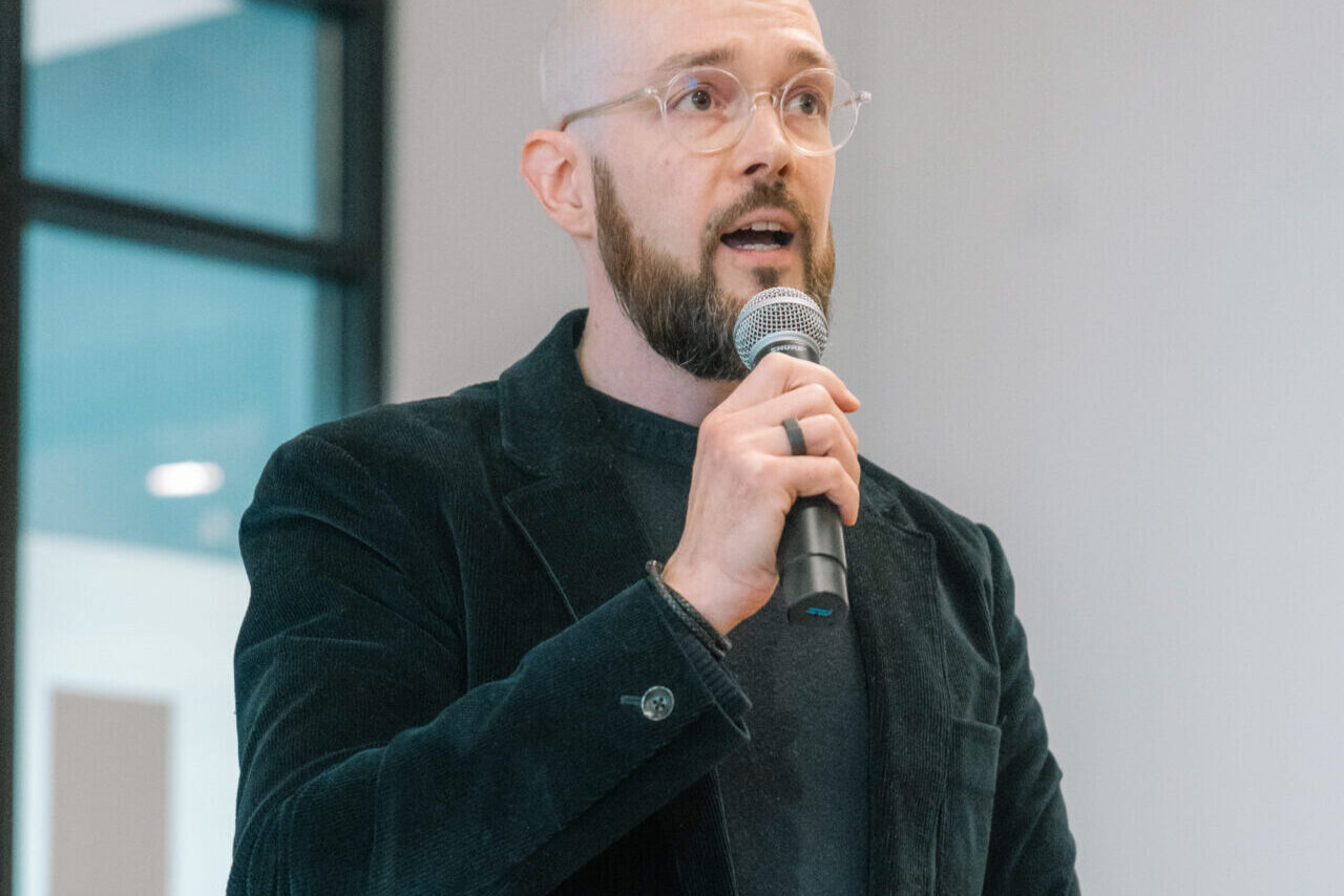 Speaker holding a microphone and phone, presenting at the Bluefors Lab opening event.